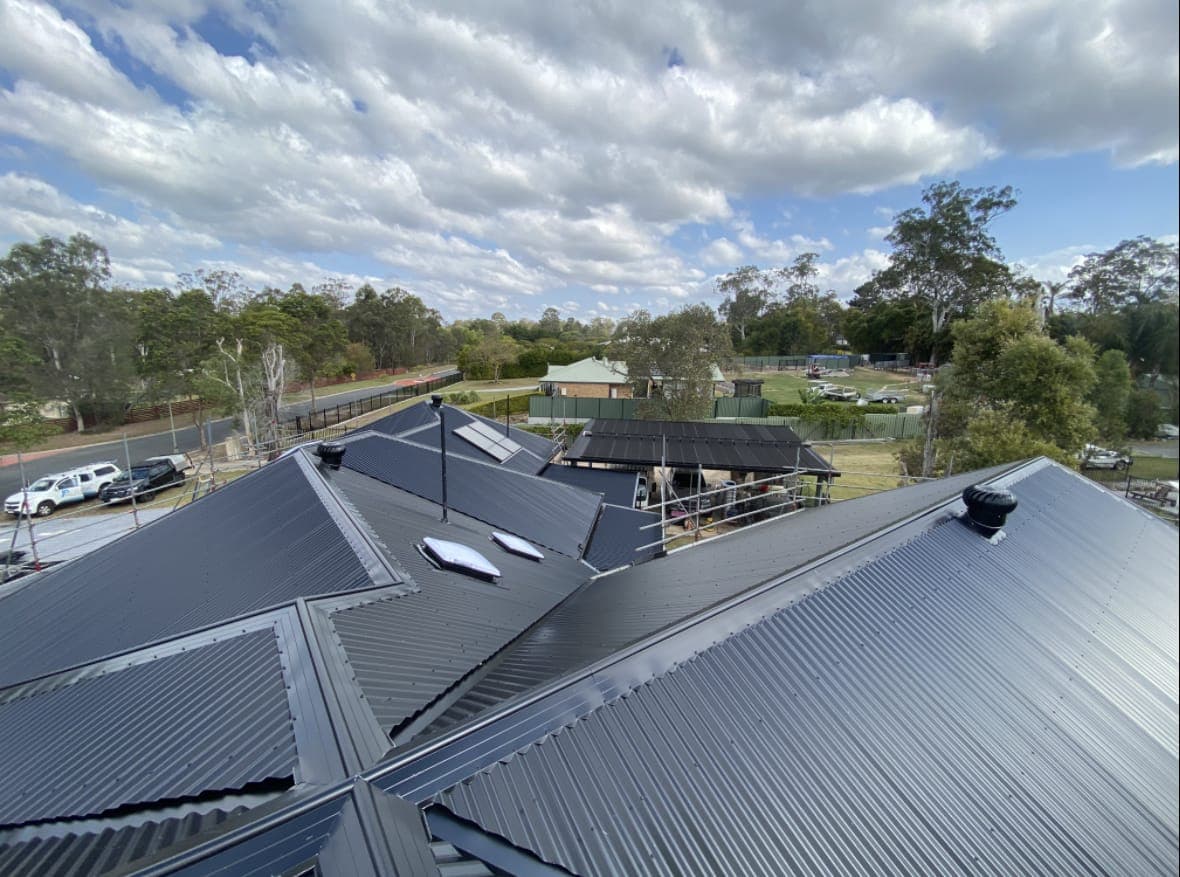 New dark grey Colorbond roof with skylights on a Brisbane home, trees and blue sky behind