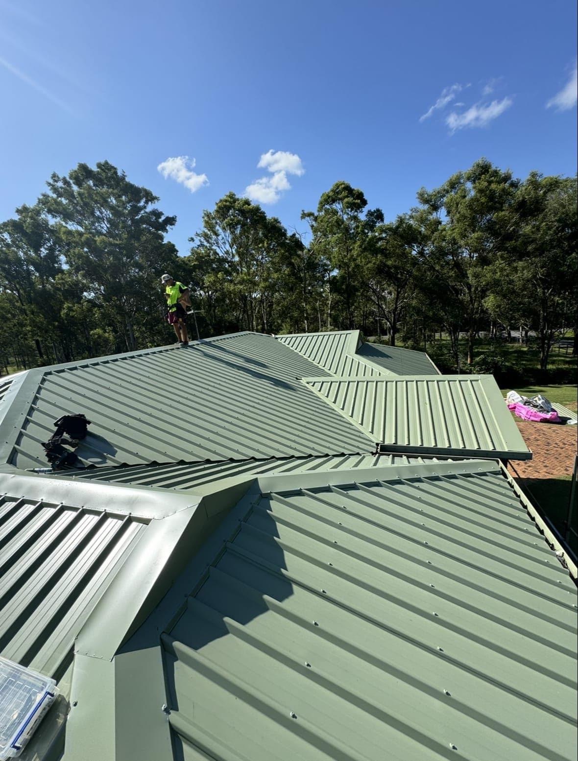 Green Colorbond roof sections meeting at new valleys, with a roofer on the ridge